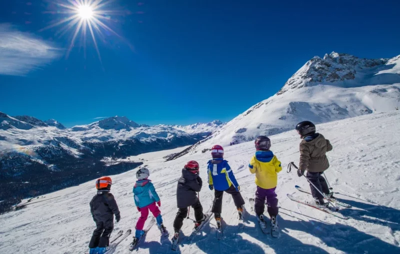 Een groep kinderen staat op de skilatten te kijken naar het omliggende berglandschap. Hun school liet sneeuwklassen organiseren door SnowCompanion.