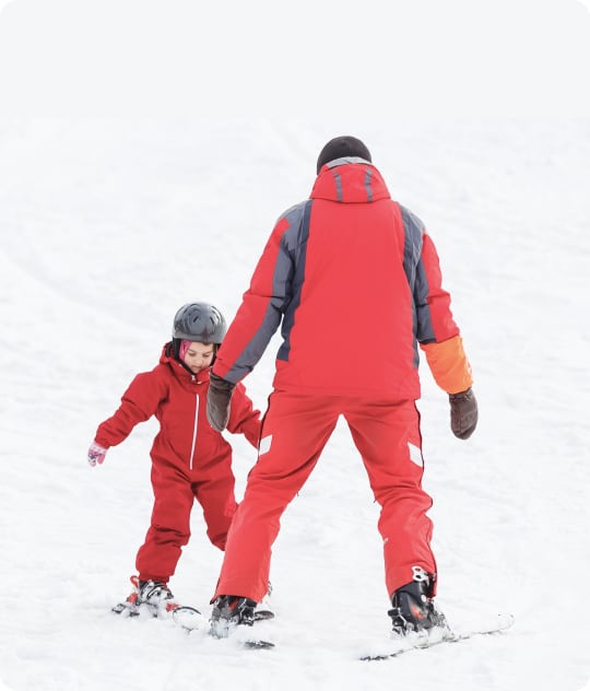 Een kind volgt snowboard- en skilessen bij SnowCompanion. Een monitor doet het voor. Ze dragen allebei rode skikleren.