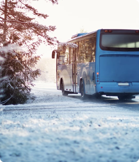 Een blauwe bus die het vervoer voor een skireis voor zich neemt. De bus bevindt zich op een besneeuwde weg.