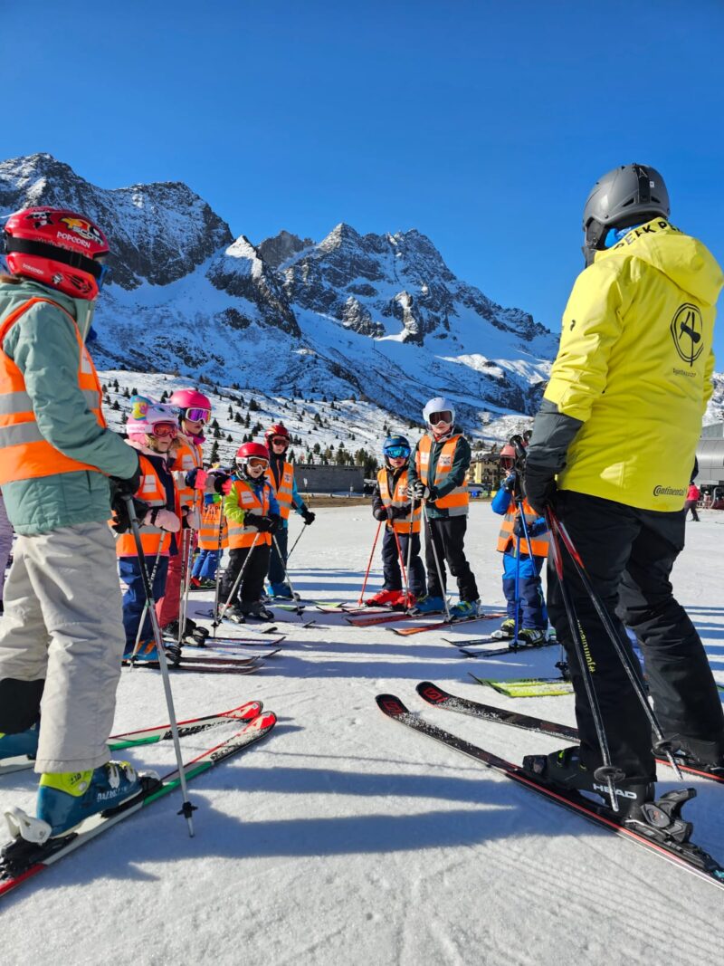 Een groep kinderen of leerlingen zijn op sneeuwklassen in Oostenrijk met SnowCompanion, waar ze Nederlandstalige skilessen voor kinderen krijgen. Ze staan in een groep en dragen allemaal oranje fluohesjes.